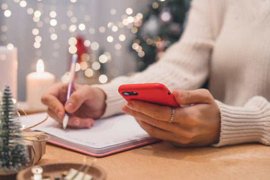 a festive background with a woman holding a phone in one hand and writing a list with the other